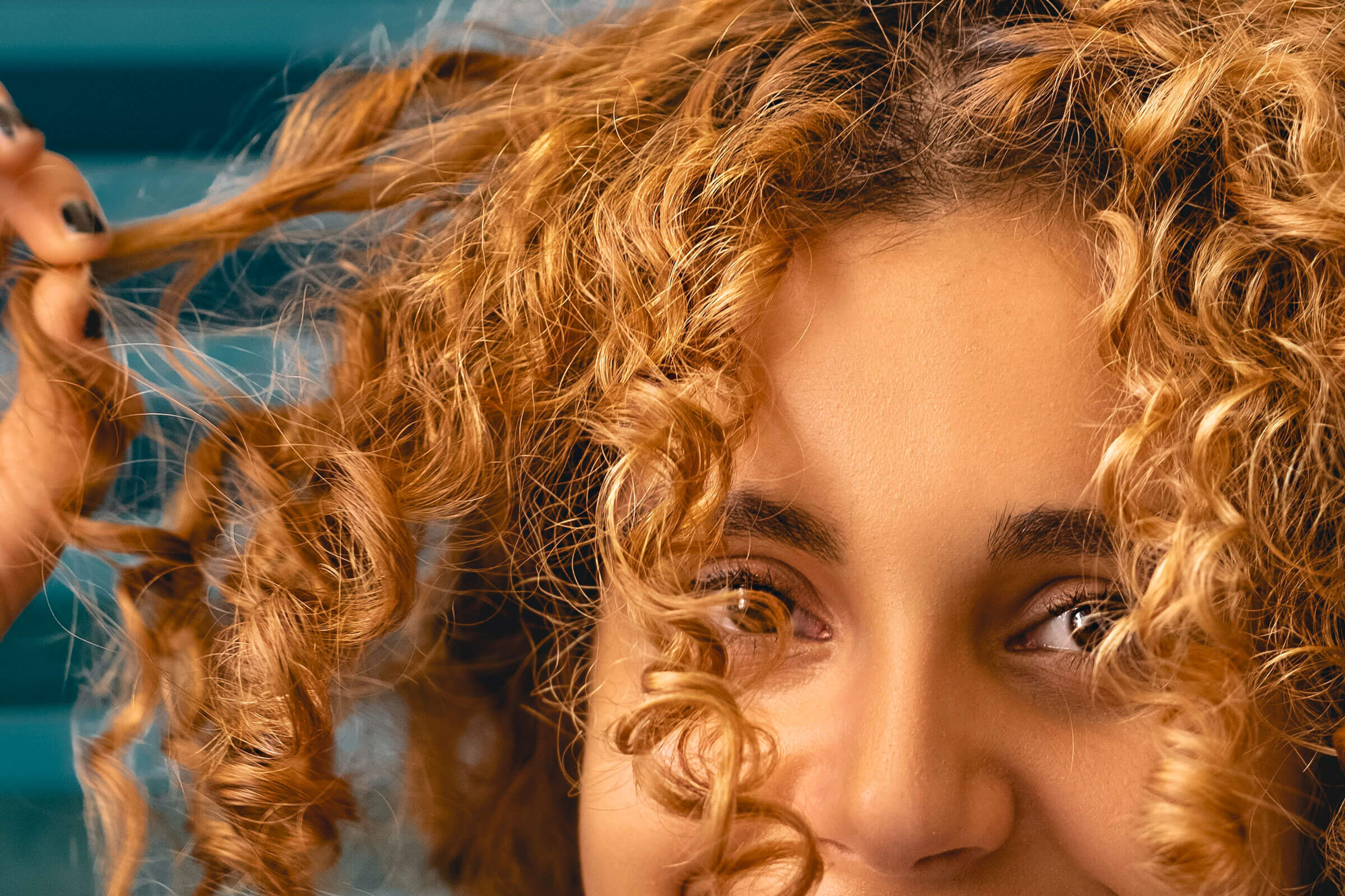 A woman with tightly curled light-brown hair tugs on one of her curls.