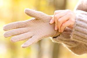 A person pulls on a beige glove over one hand.