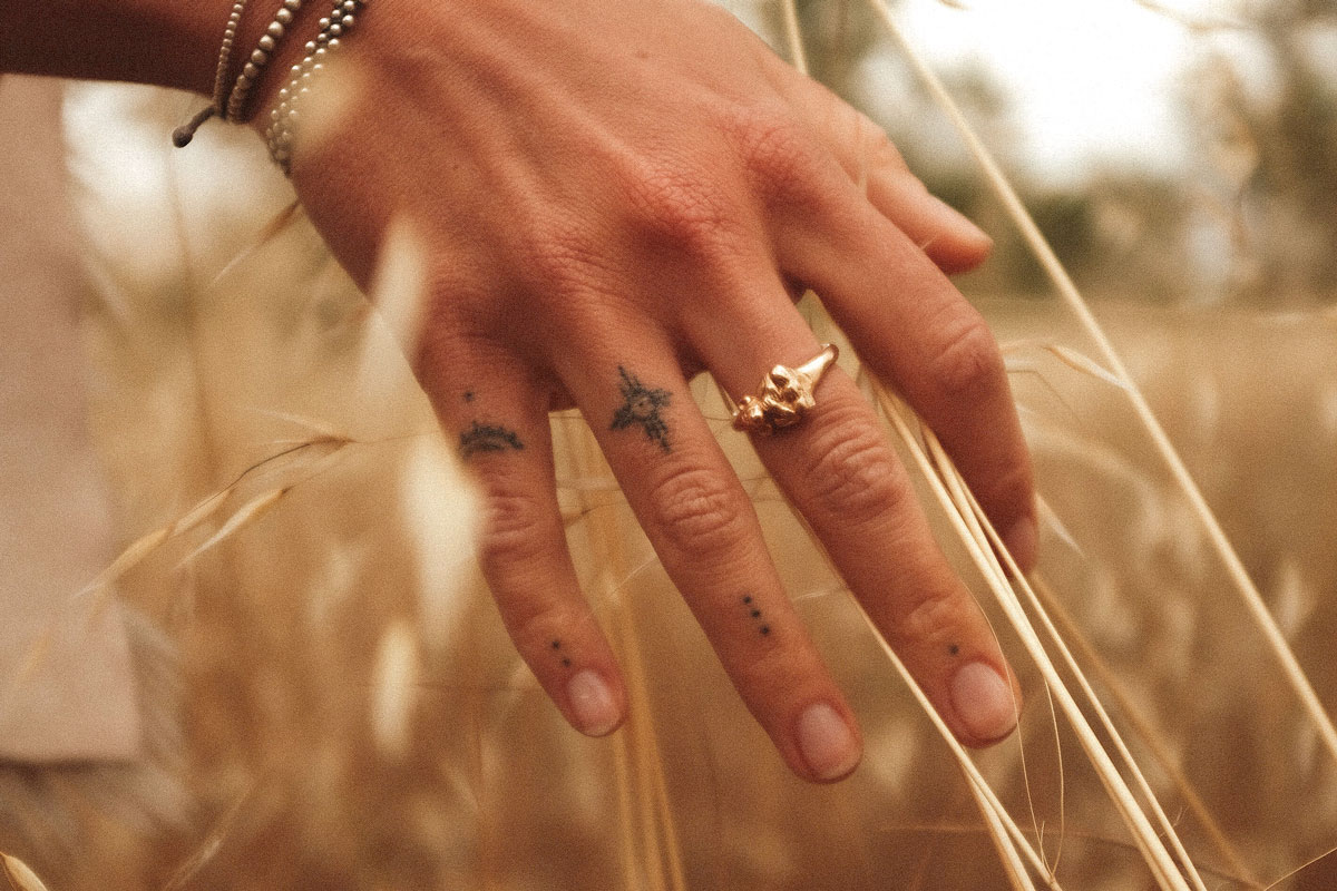 A close-up image of a hand with small, minimalist tattoos on the fingers.