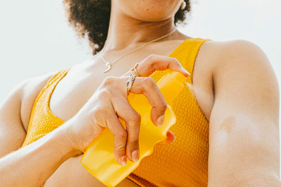 A woman sprays sunscreen on her arm.