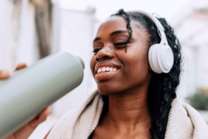 black woman wearing headphones drinking out of a water bottle