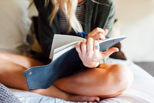 Low section of woman writing diary while sitting on bed