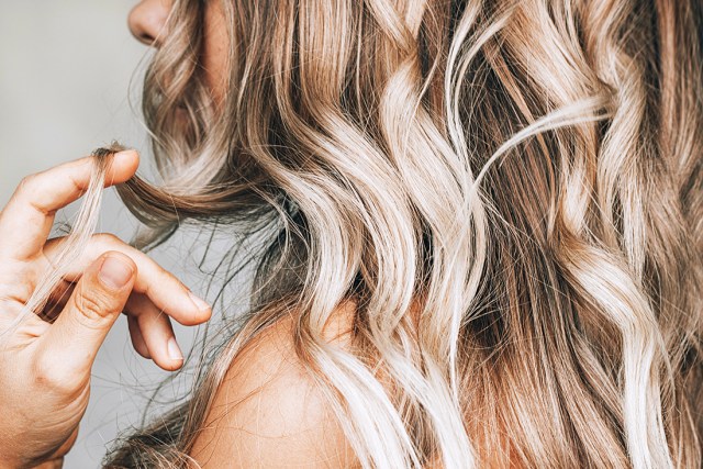 A young blonde woman with the wavy hair holding a lock of hair in her hand