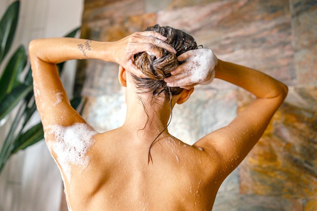 Back view of naked young woman washing her hair while taking shower in bathroom