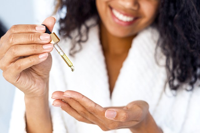 Woman wearing white bathrobe using oil dropper in her hands