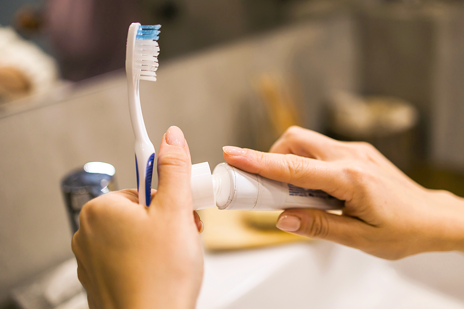 Female hand holding toothbrush with toothpaste applied on it in bathroom