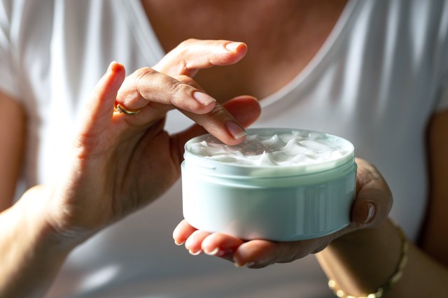 Woman putting her finger in jar of cream