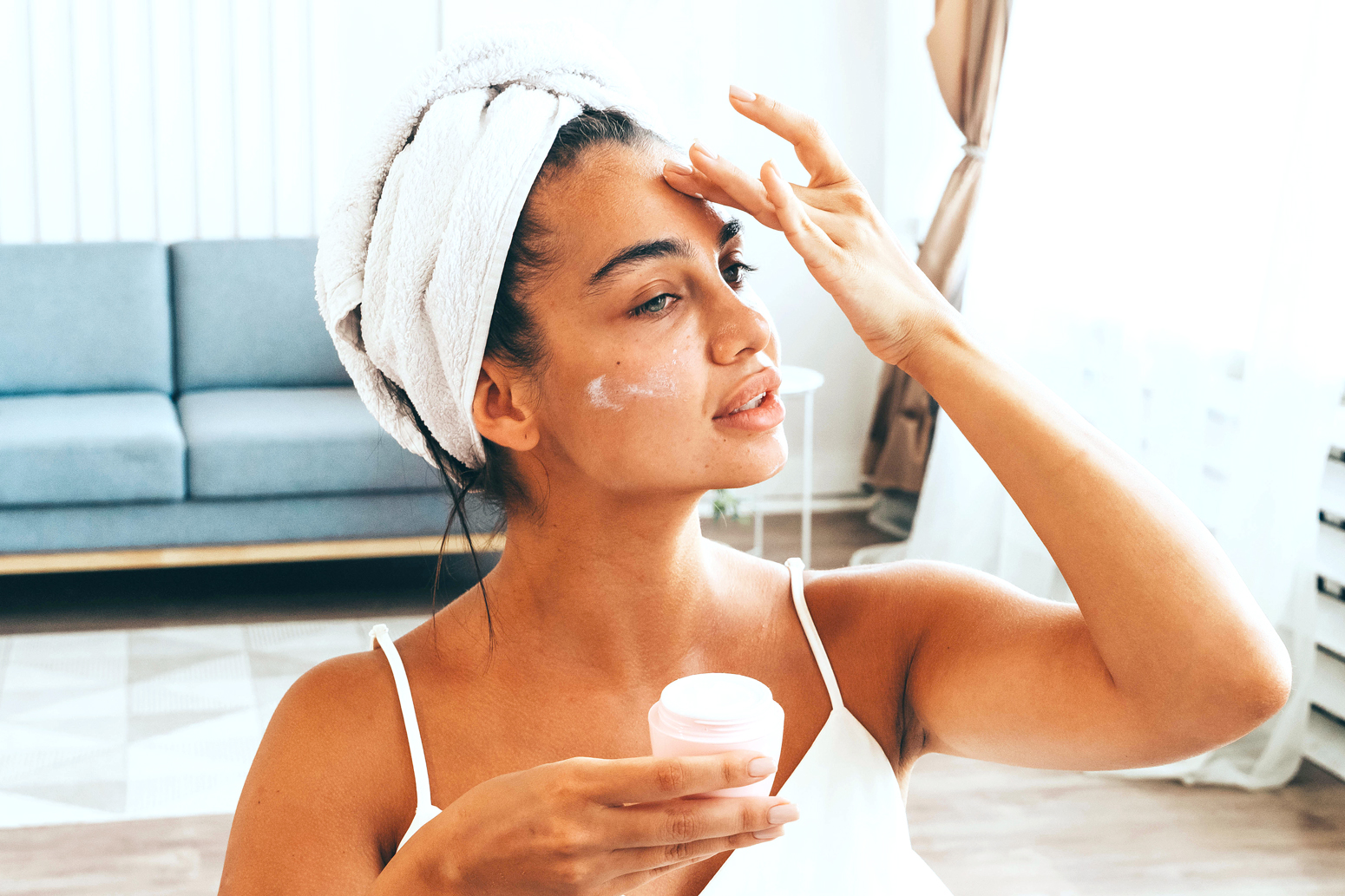 Woman with towel on her head applying skin care product to her face