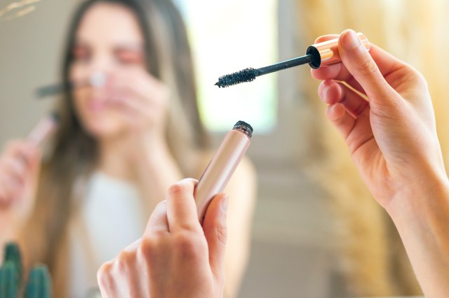 Woman holding mascara tube in her hands, in front of a mirror