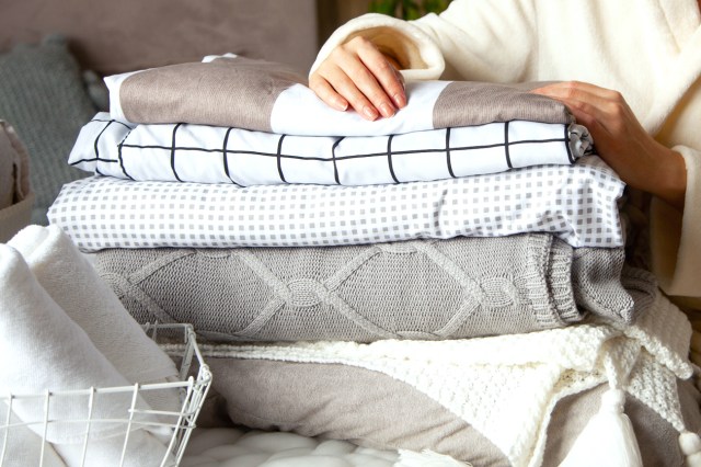 Woman holding folded bedding, sheets, blankets, with towels in foreground