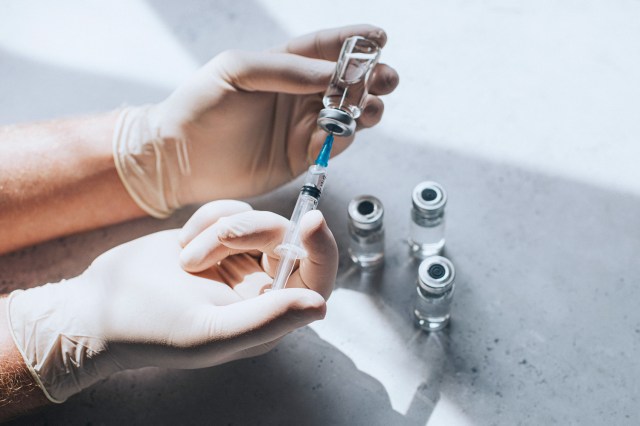 The medical professional uses the syringe to extract the medicine from the glass bottle.