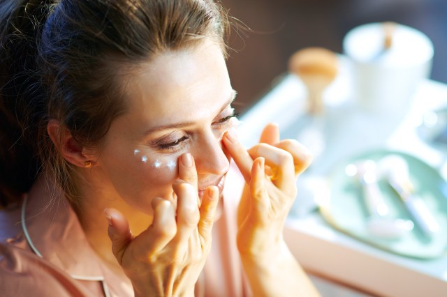 Female at home on sunny day applying eye cream with her fingers