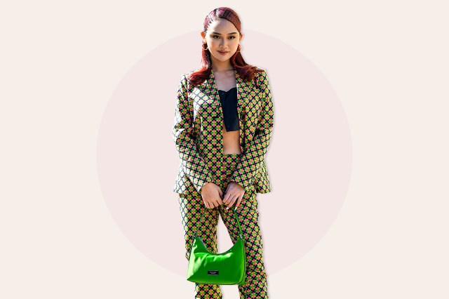 A guest wears gold earrings, a black V-neck / cropped top, a green / pink / yellow / black print pattern blazer jacket