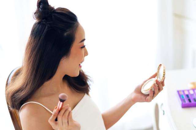 Woman looking in compact mirror applying blush to her cheeks