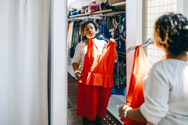 Woman looking at red dress in mirror at clothing store