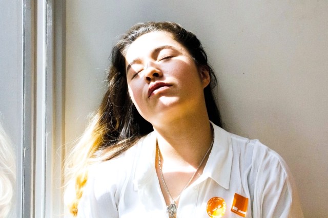 Woman with eyes closed next to a window, light coming through and shining on her face