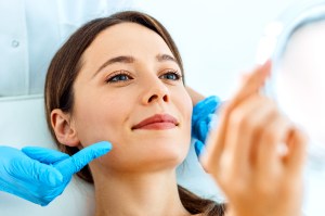 Beautiful smiling Woman having Facial Treatment looking at mirror