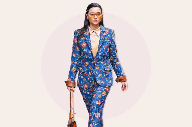 Julia Comil wears Ferragamo sunglasses, a hair brooch, a beige shirt, a floral print blue and colored blazer jacket 