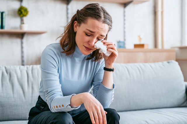 Woman sitting on a couch, crying, holding a tissue to her eye