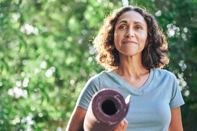 Mature woman holding yoga mat outside, smiling