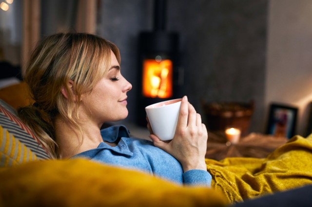 Smiling woman with cup of coffee relaxing on couch at home in the evening