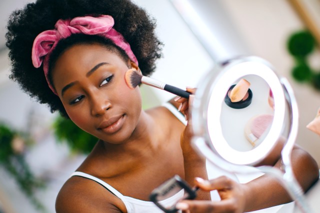 Woman applying blusher on her cheeks sitting in front of a mirror