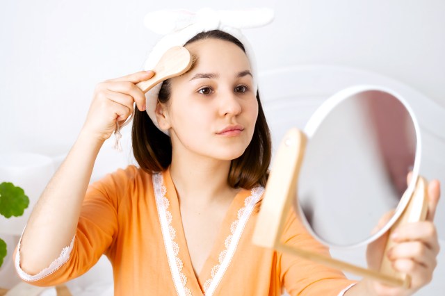 Woman dry brushing her face while holding a mirror