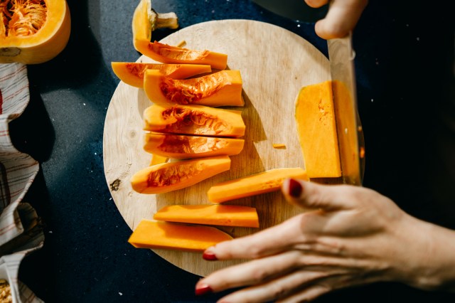 Woman slicing a Butternut Squash on a wooden cutting board.