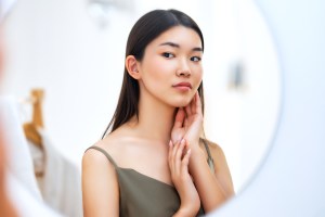 Young woman looking at herself in the mirror, touching her face