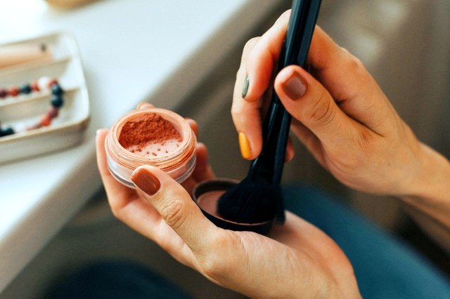 Close up of a woman using blush powder and brush