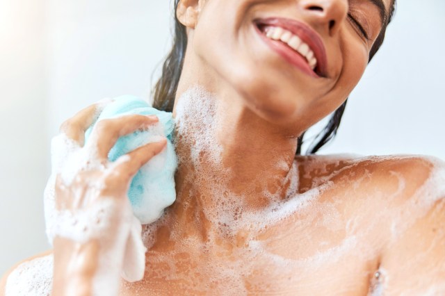 Closeup of a woman smiling, washing her body in the shower