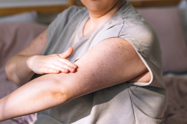 cropped image of a young woman sitting on her bed applying body lotion on her arms