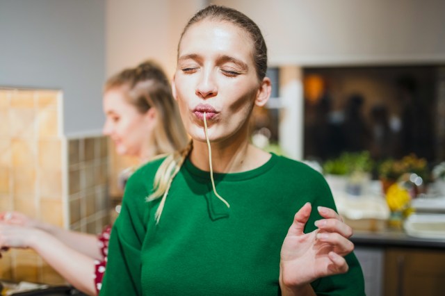 Young woman poses for the camera with spaghetti hanging out her mouth