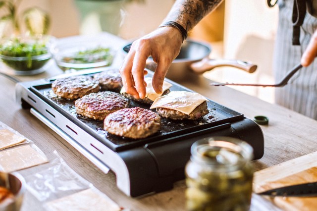 Man putting cheese on meat while making cheeseburgers on electric grill