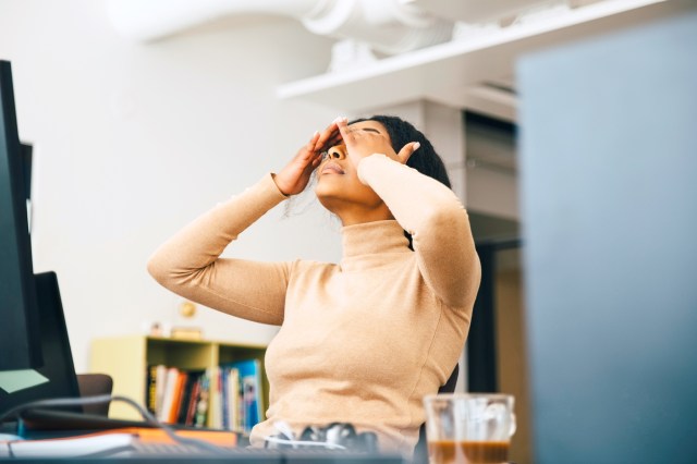 Woman rubbing her face, frustrated, sitting at a computer