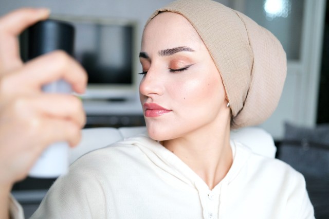 Young woman, wearing makeup, spraying her face with beauty product