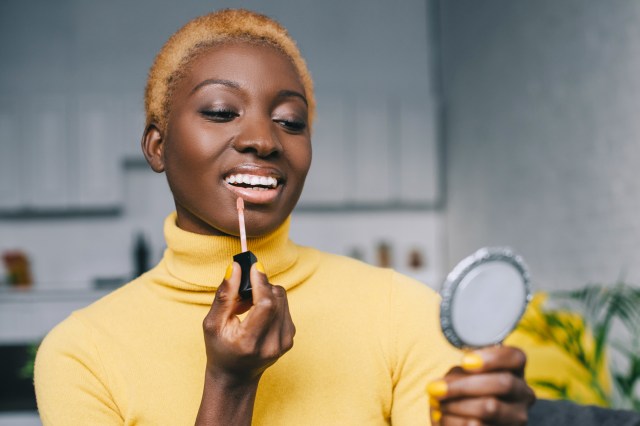 Woman applying lip gloss and looking in mirror