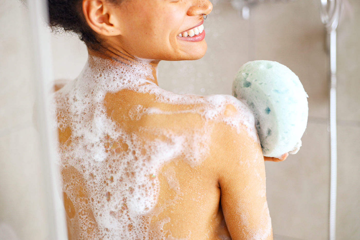 Woman showering, using a sponge to wash her back