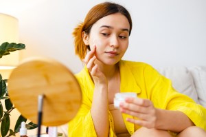 Woman putting cream on her face, skin care routine