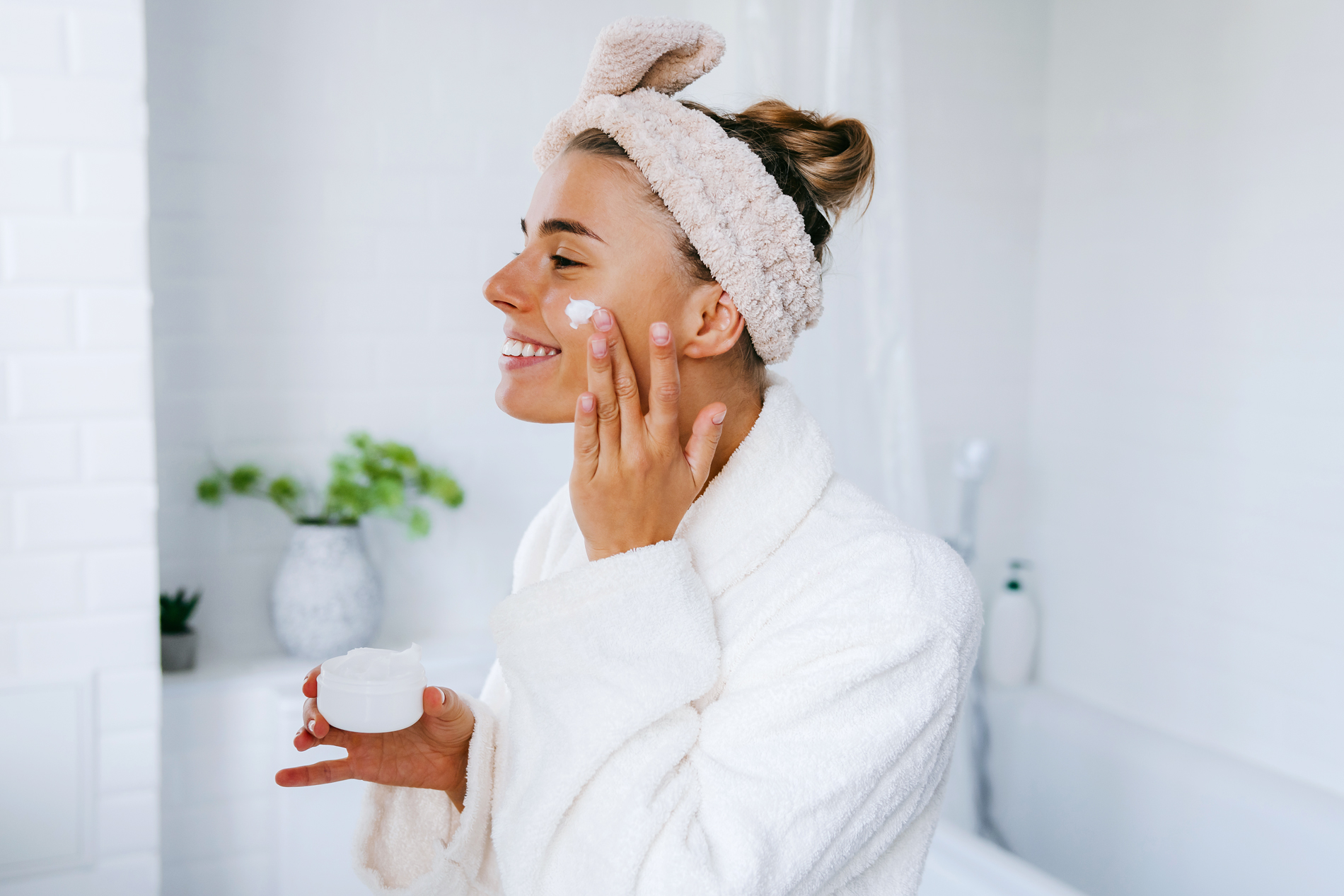 Woman applying face moisturizer in bathroom